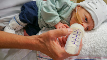 Baby ligt op de zij en drinkt uit een flesje